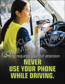 A safety poster showing a female driver in a high-visibility vest holding a smartphone while behind the wheel of a truck, with text stating "Driving requires your full attention. NEVER USE YOUR PHONE WHILE DRIVING."